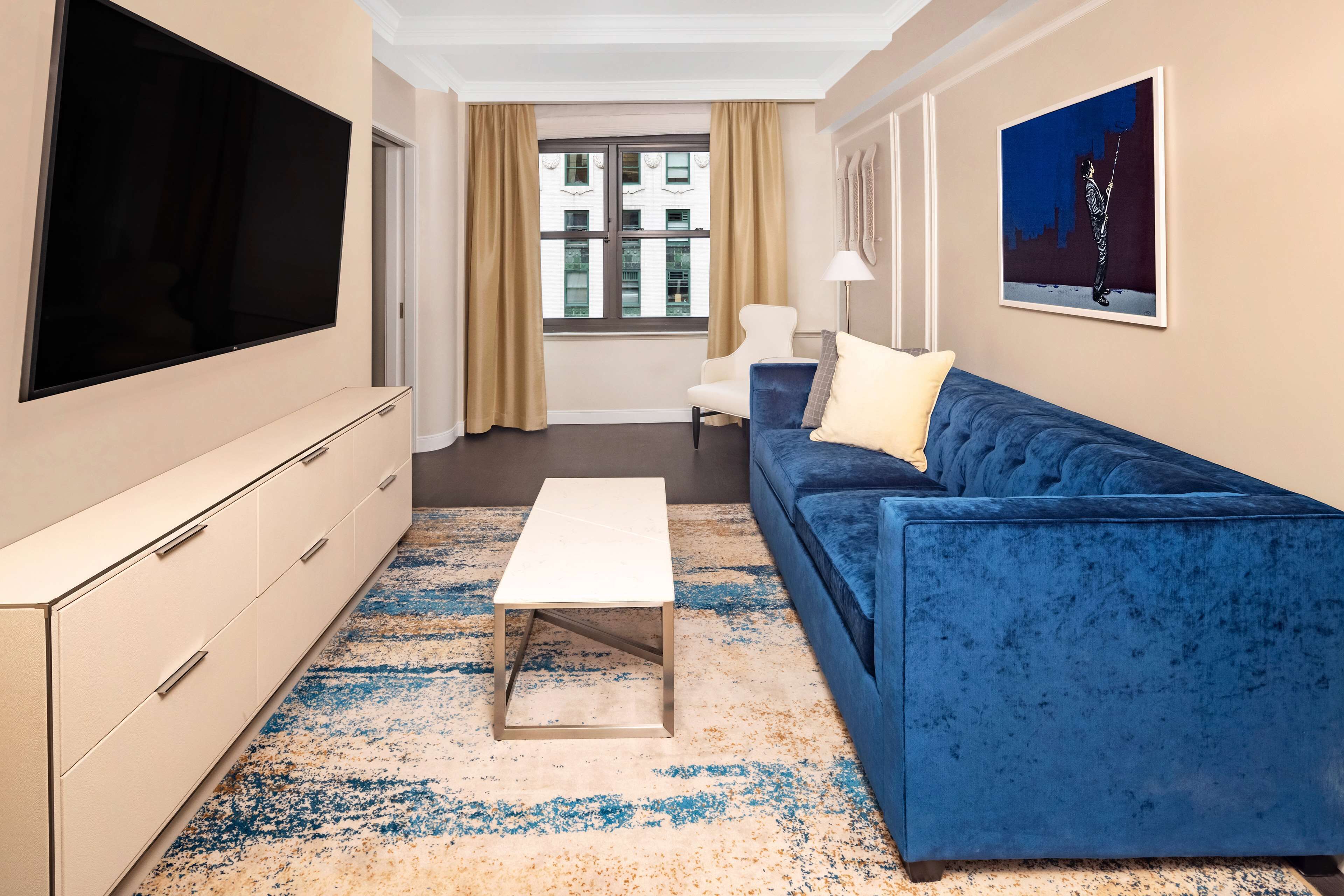 A modern living room with a large flat-screen TV, a blue sofa, a white coffee table, and a beige cabinet.