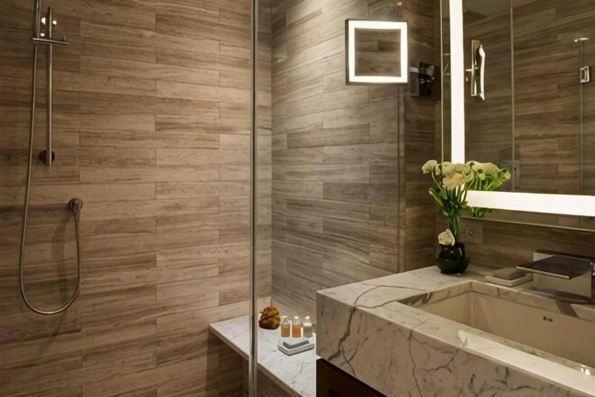 Een badkamer met een marmeren wastafel, een douchecabine met glazen wanden en een vaas met bloemen.