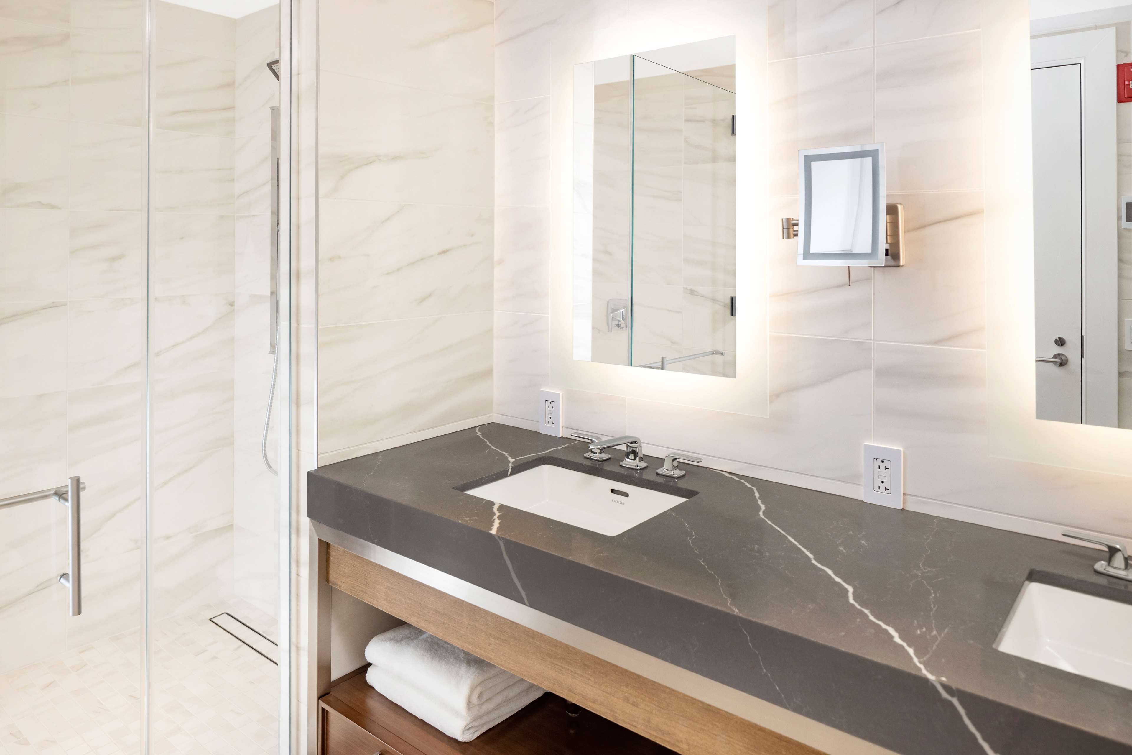 A modern bathroom with a marble vanity, a large mirror, and a glass shower enclosure.