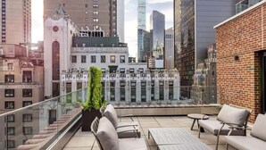 A rooftop terrace with outdoor seating, a view of city buildings, and a decorative wall. - Hilton Club The Quin New York (New York)