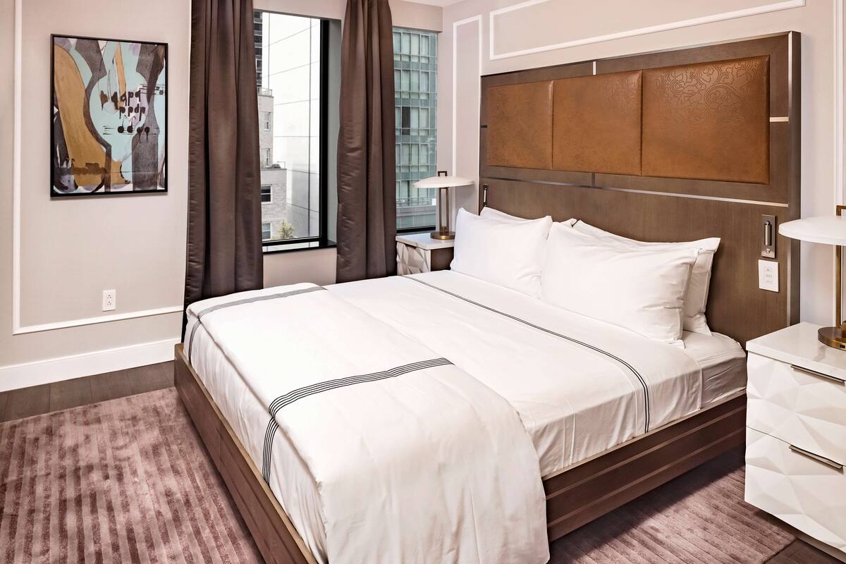 Hotelkamer met een groot bed, nachtkastje, lamp en raam met gordijnen.