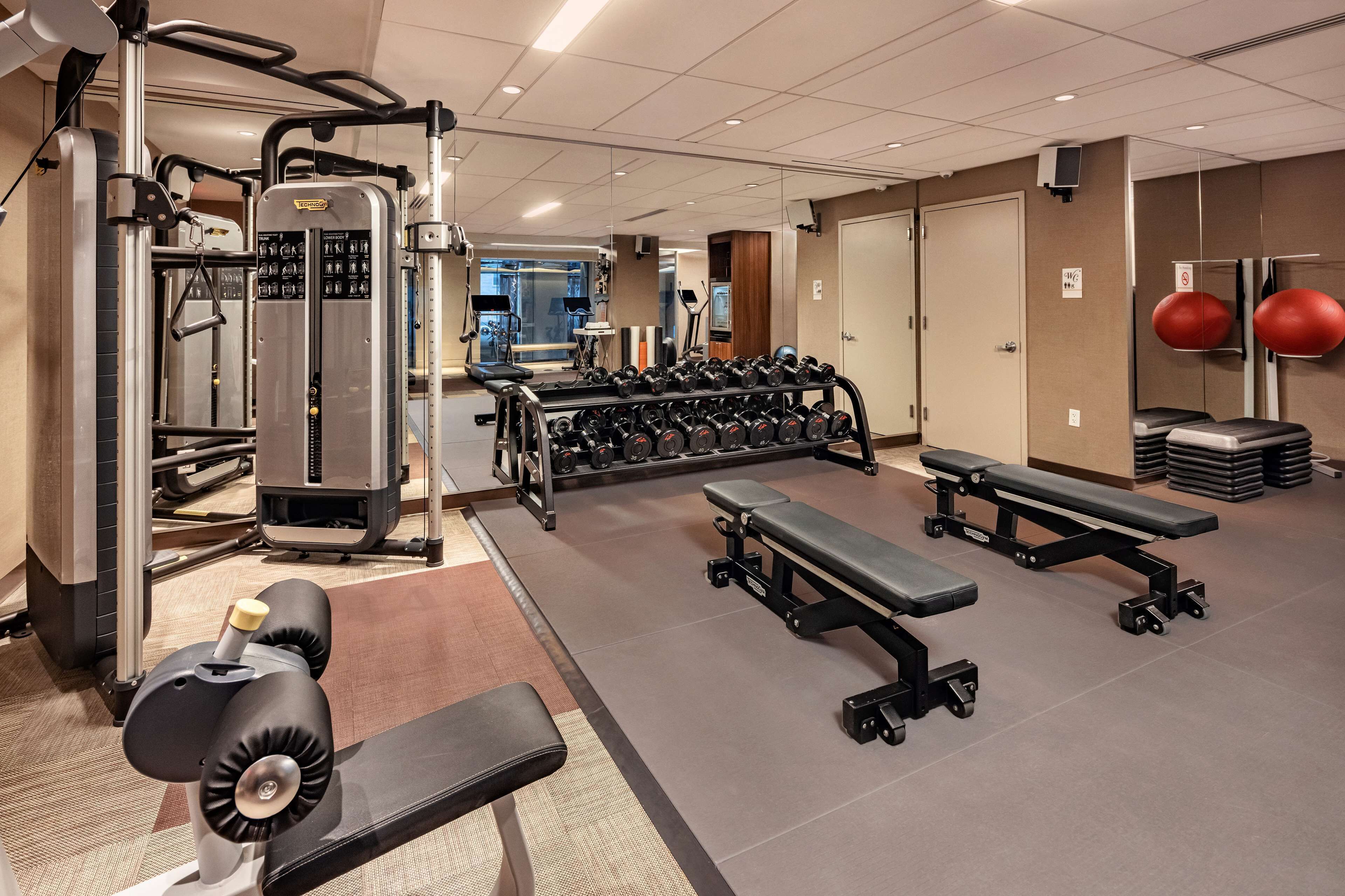 Un gimnasio con máquinas de pesas, mancuernas, bancos y pelotas de ejercicio.