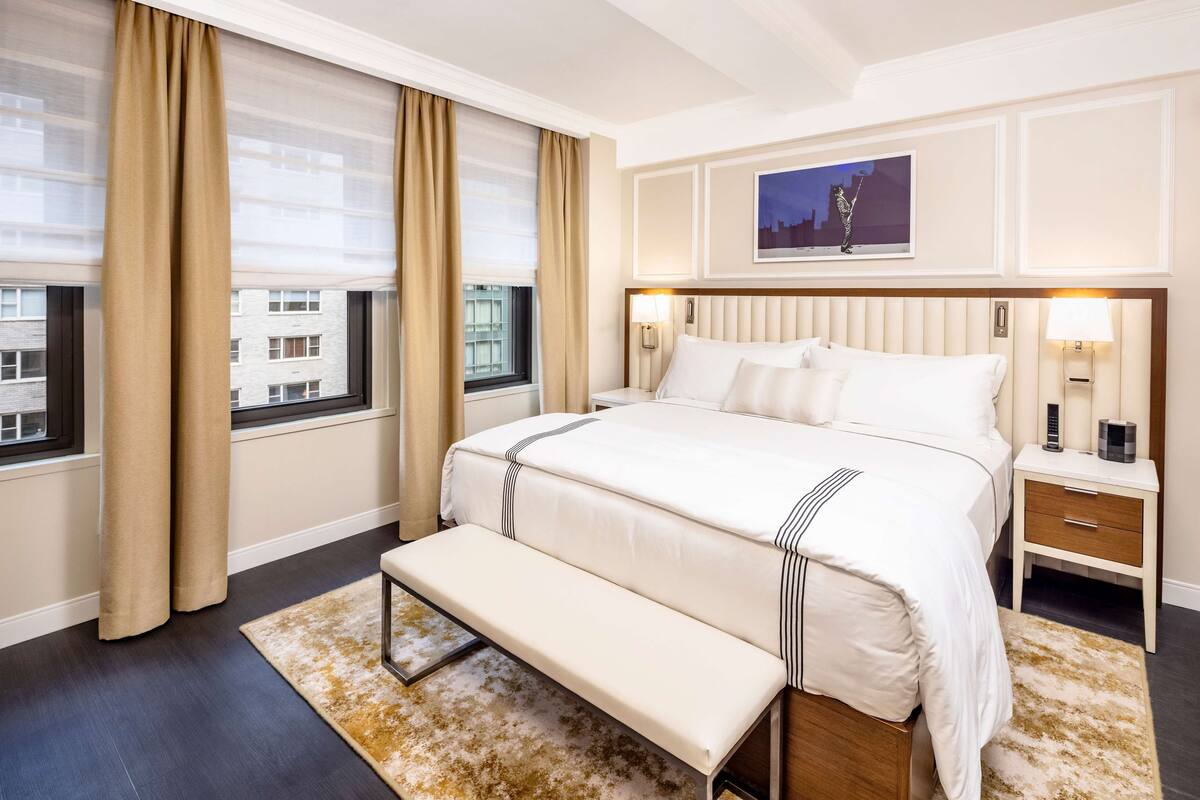 Hotelkamer met een groot bed, een bankje, een nachtkastje en uitzicht op gebouwen door het raam.