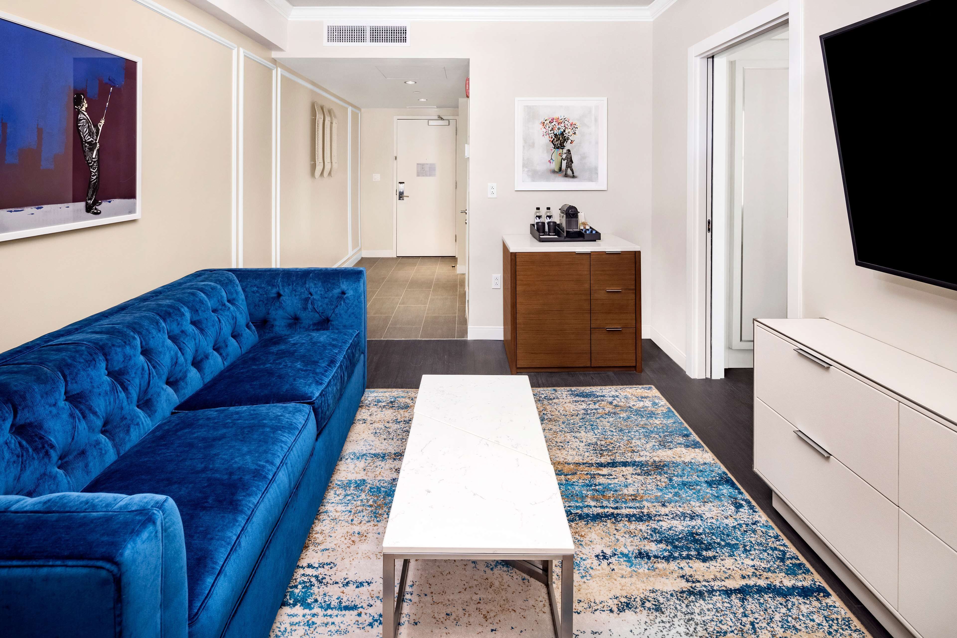Una sala de estar moderna con un sofá azul, una mesa de centro blanca y un televisor en la pared.