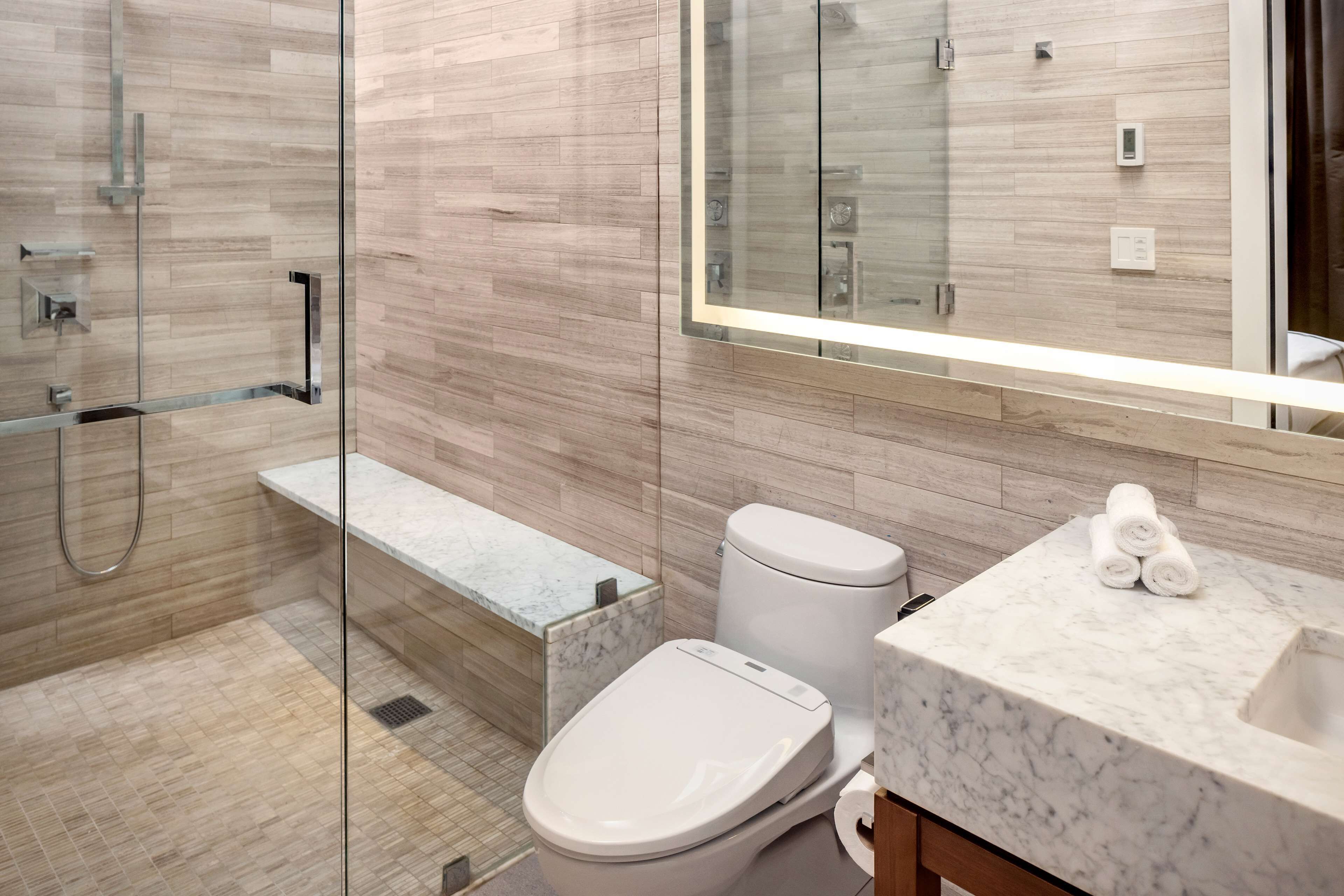 A modern bathroom with a glass shower enclosure, a marble sink, and a toilet.