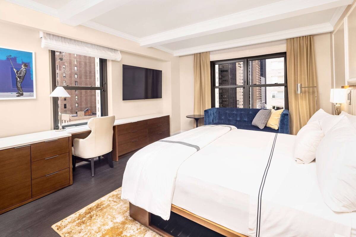 Een hotelkamer met een groot bed, een bureau met stoel, een aan de muur bevestigde televisie en een raam met gordijnen.
