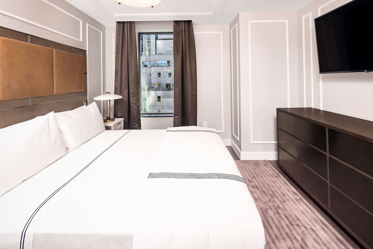 Een hotelkamer met een groot bed, een televisie, een dressoir en een raam met gordijnen.