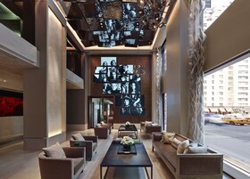Een moderne lobby met een centraal zitgedeelte, een wand met ingelijste foto’s en uitzicht op de straat door grote ramen.