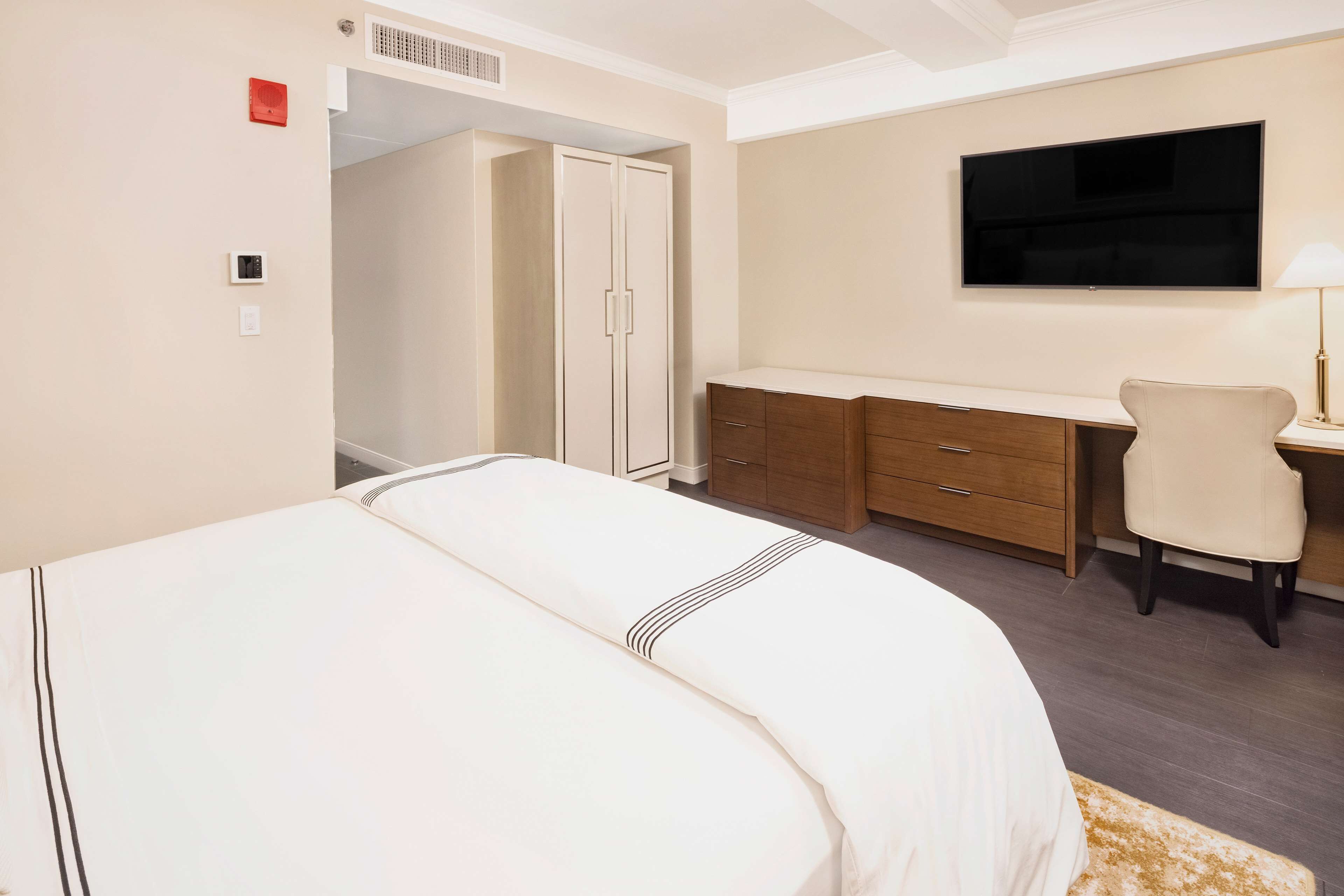 A hotel room with a bed, a desk, a chair, a wardrobe, and a TV on the wall.