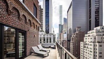 Una terraza en la azotea con sillones de descanso, un edificio de ladrillo y modernos rascacielos al fondo.
