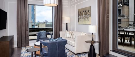 Una sala de estar moderna con un sofá, un sillón y una mesa de centro, un televisor de pantalla plana y un ventanal con vistas a la ciudad.