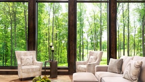 A room with large windows, a sofa, two armchairs, a coffee table, and a side table with a lamp. - Nemacolin (Farmington)