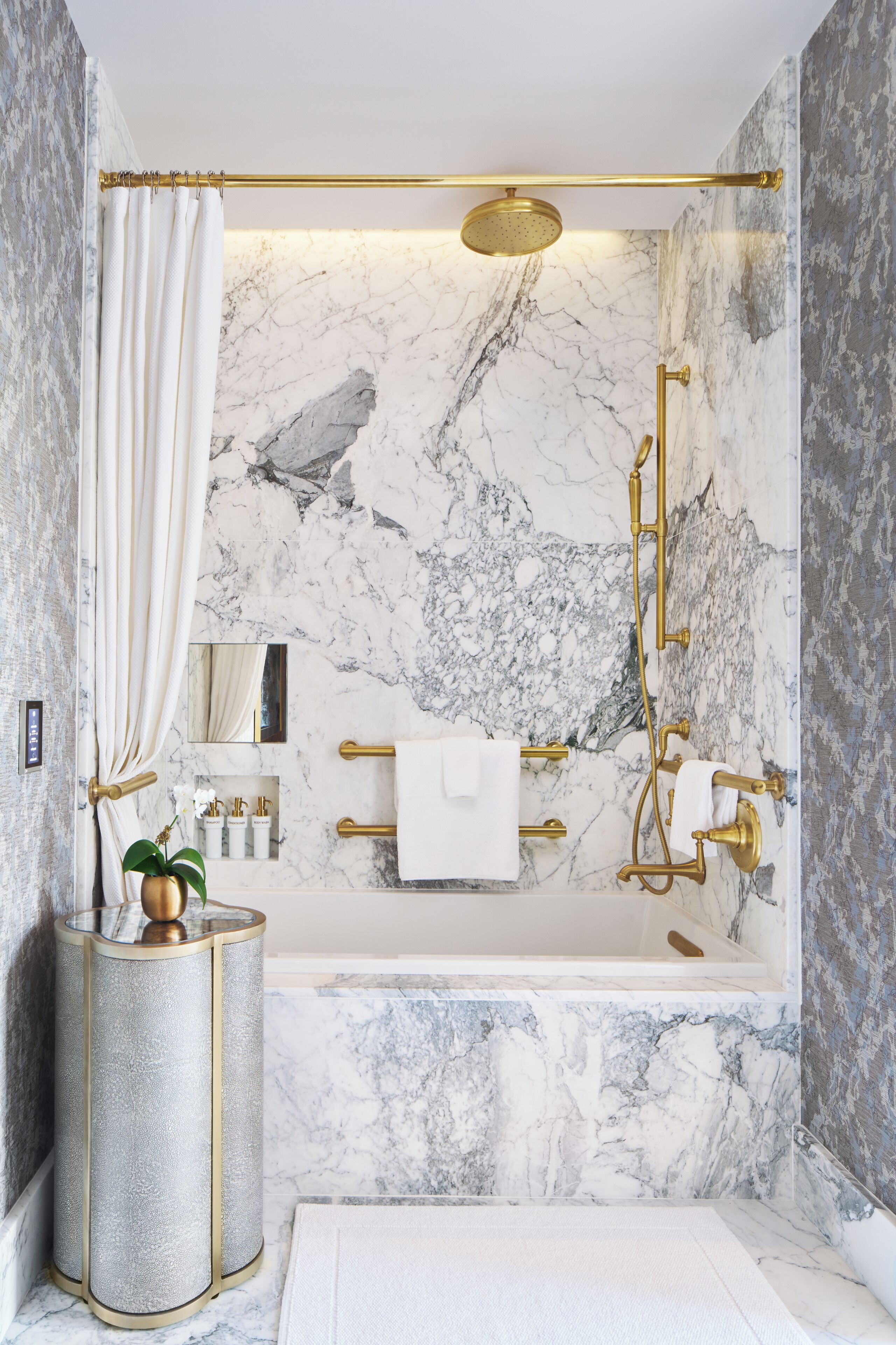 Ein modernes Badezimmer mit Marmorwand, einer Badewanne, einer Dusche mit goldener Brause und einem WC mit Goldarmatur.