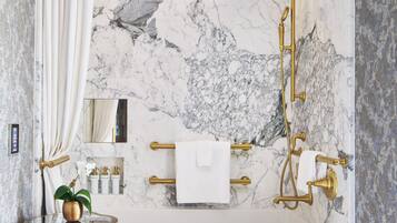 Ein modernes Badezimmer mit Marmorwand, einer Badewanne, einer Dusche mit goldener Brause und einem WC mit Goldarmatur.