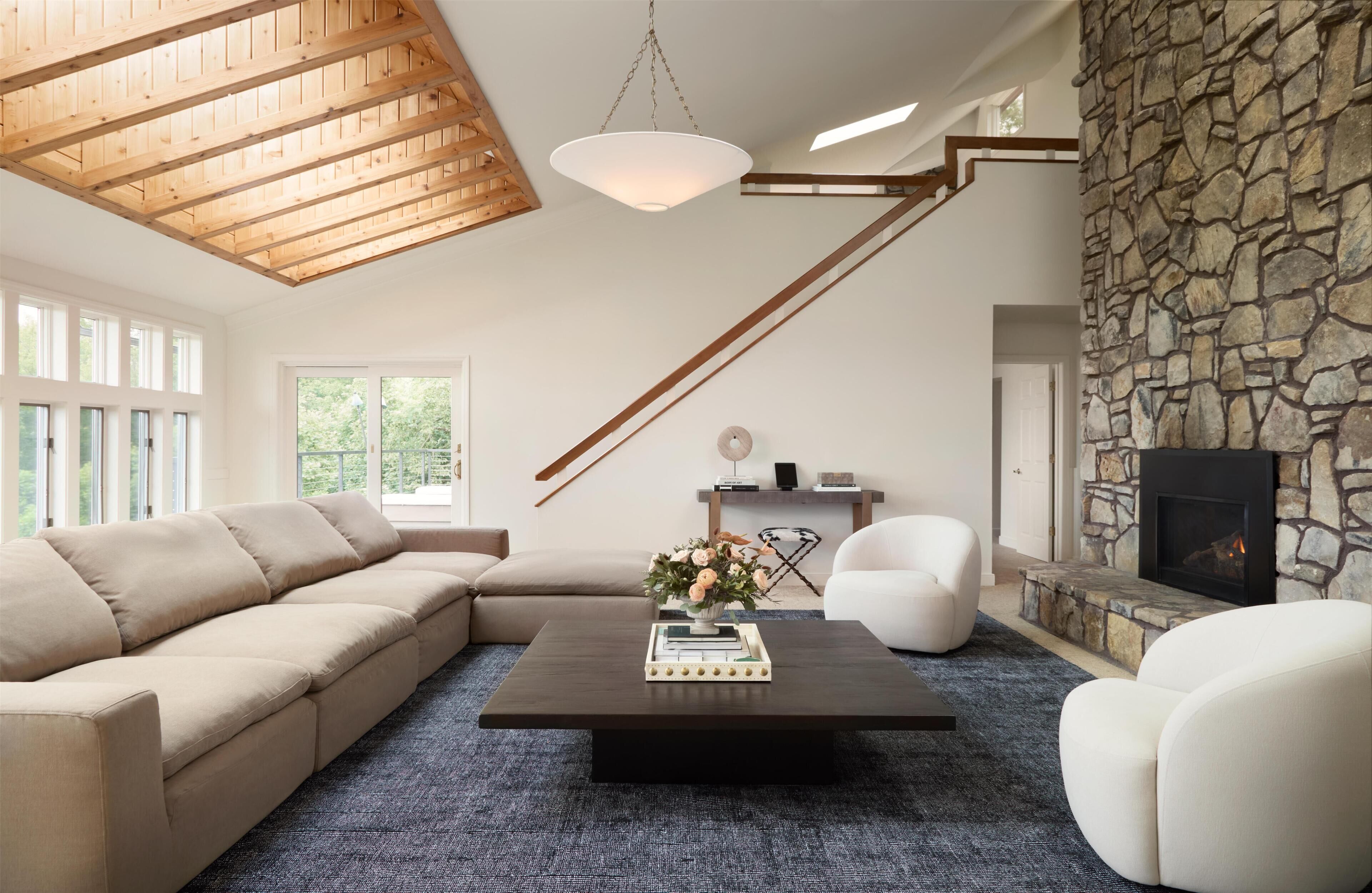 A modern living room with a sectional sofa, a coffee table with books and flowers, a fireplace, and a stone accent wall.