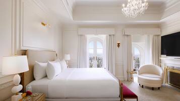 A hotel room with a large bed, a chandelier, a television, and a view of the outdoors.