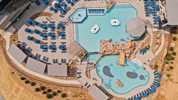 An aerial view of a resort with multiple swimming pools, sun loungers, and a landscaped area with rocks and shrubs. - Nemacolin (Farmington)