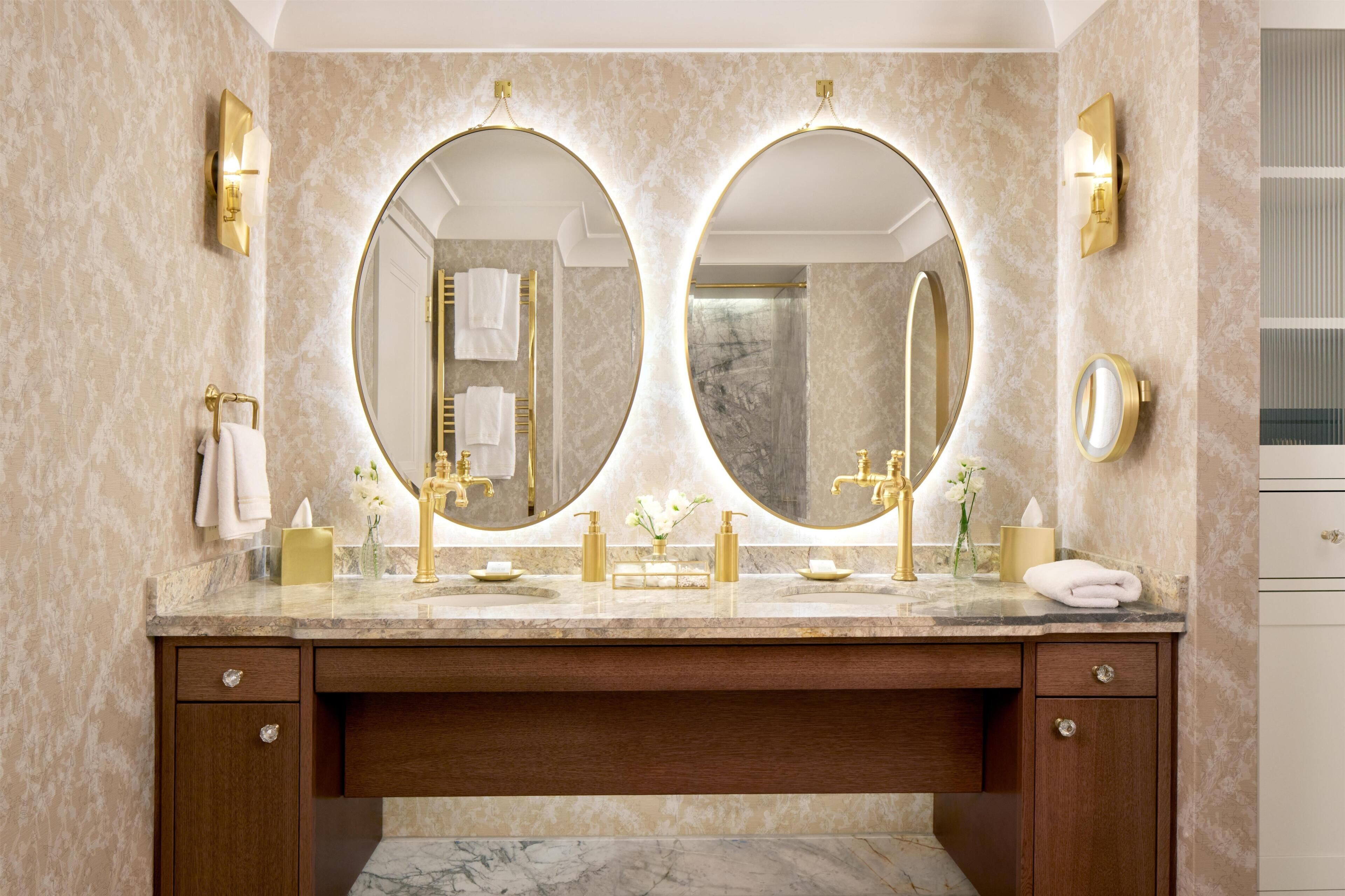 A bathroom with two large mirrors, a marble countertop, gold fixtures, and a wooden vanity.