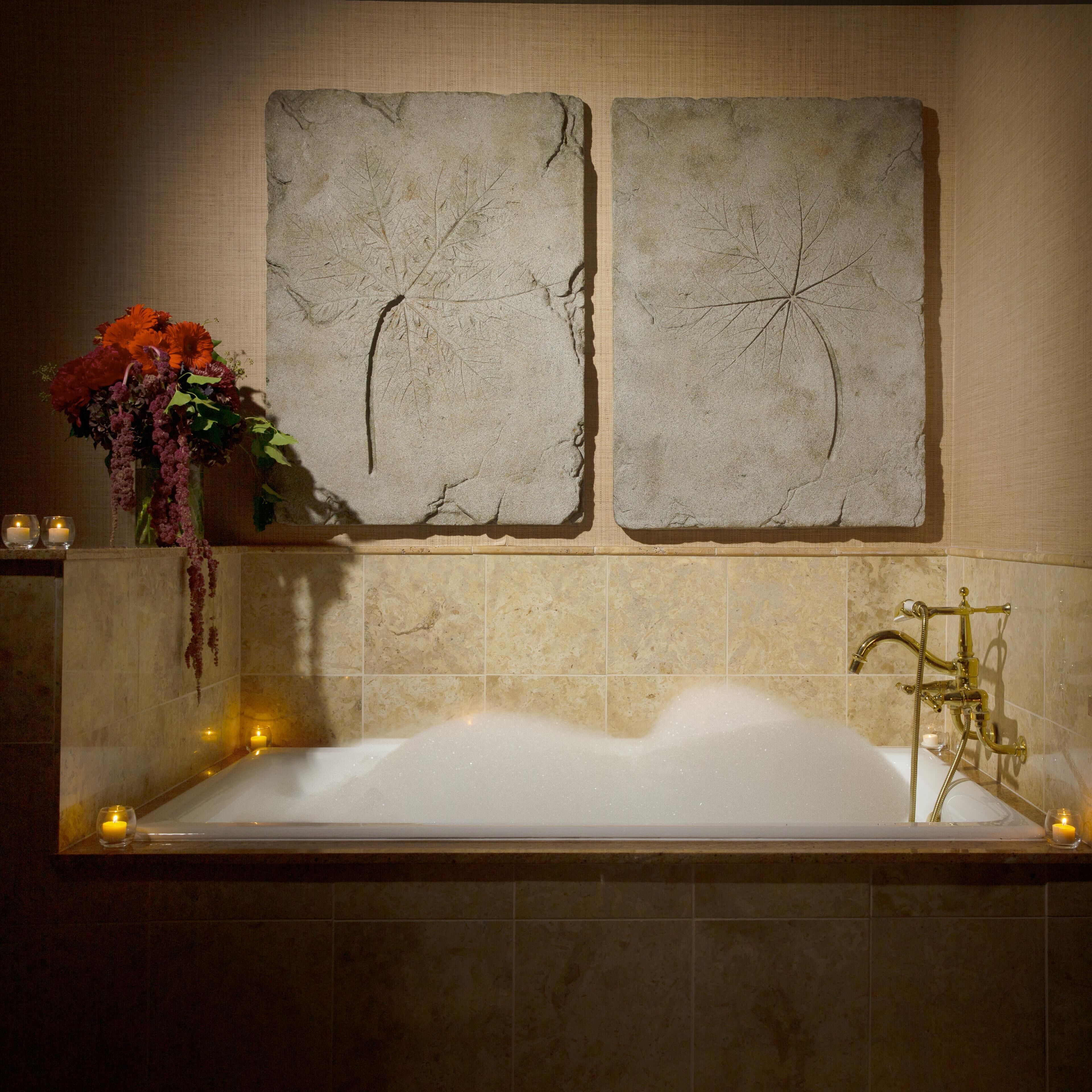 Un baño con bañera, dos obras de arte colgadas en la pared, un florero con flores y velas.