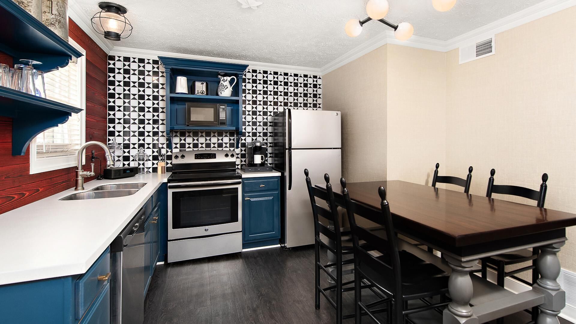 A modern kitchen with blue cabinets, a black and white patterned backsplash, stainless steel appliances, and a wooden dining table with chairs.