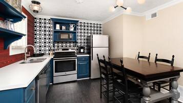 Une cuisine moderne avec des meubles bleus, un crédence à motifs noir et blanc, des appareils en acier inoxydable et une table à manger en bois avec des chaises.