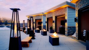 An outdoor patio area with fire pits and seating, connected to a building with stone and wood exterior. - Nemacolin (Farmington)