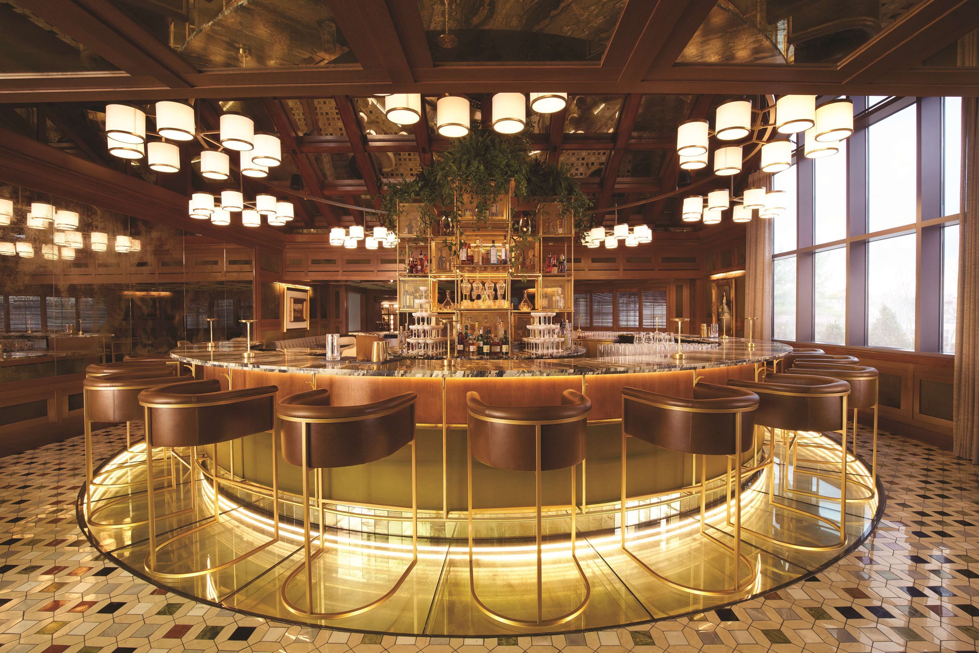 Una zona de bar con barra circular, varios taburetes e iluminación colgante.