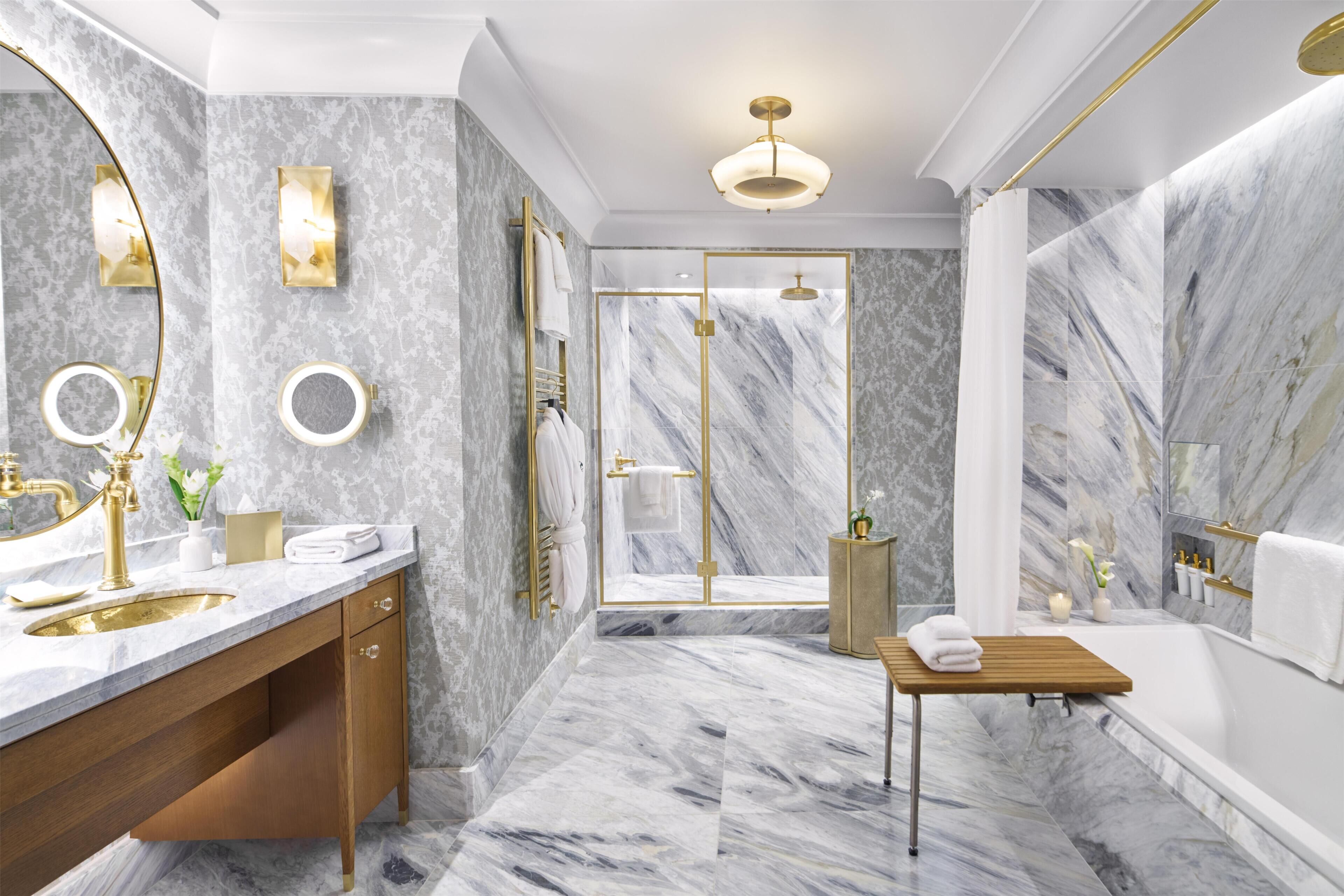 A luxurious bathroom with marble floors, a gold vanity, a freestanding bathtub, and a glass-enclosed shower area.