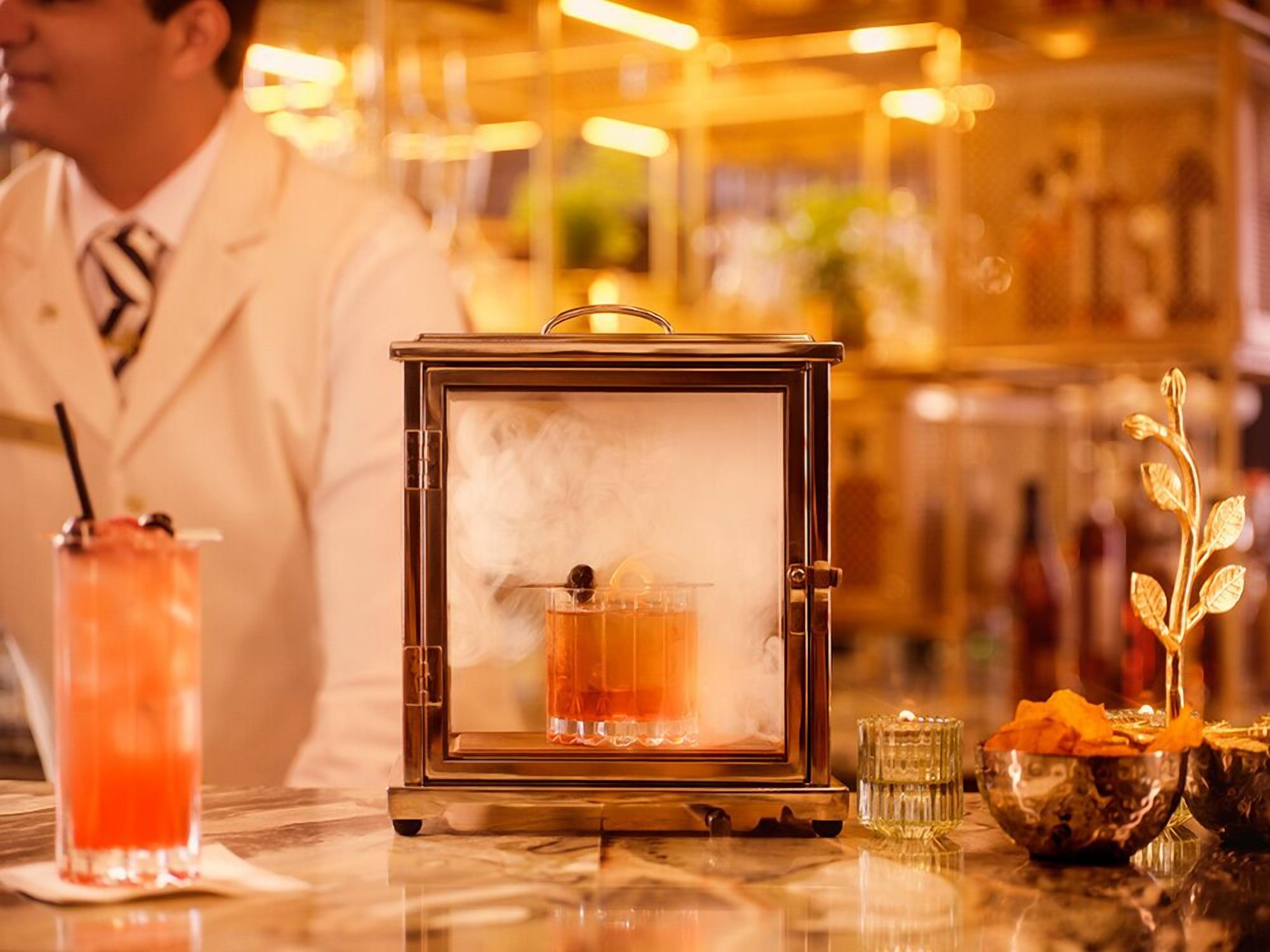 Un bar con camarero, un cóctel y un objeto decorativo.