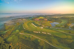 An aerial view of a golf course with bunkers, a clubhouse, and a pond.