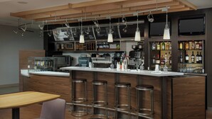Un espace bar moderne avec un long comptoir, des tabourets, une machine à café et un téléviseur fixé au mur.