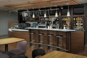 Un área de bar moderna con una barra larga, taburetes, una máquina de café y un televisor montado en la pared.
