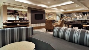 Un hall d’hôtel moderne doté d’un espace salon, d’un bar et d’un téléviseur fixé au mur.