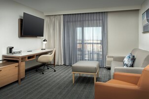 Habitación de hotel con televisión de pantalla plana, escritorio con silla, sofá y ventana con cortinas.