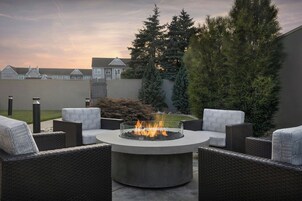 Un espacio de estar al aire libre con muebles de mimbre y una chimenea central.