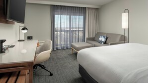 Une chambre d’hôtel comprenant un lit, un bureau, une chaise, un canapé, une télévision, une lampe et une fenêtre avec des rideaux.