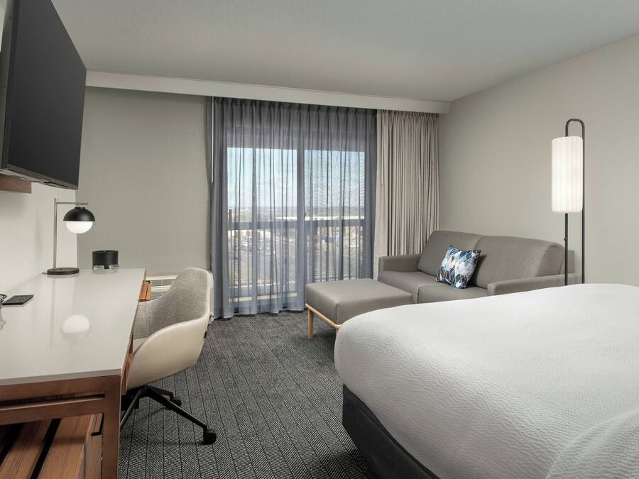 A hotel room with a bed, a desk, a chair, a sofa, a TV, a lamp, and a window with curtains.