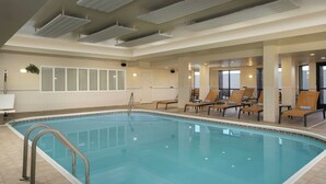 Une grande piscine intérieure avec un sol carrelé, un escalier métallique pour y accéder et plusieurs chaises longues disposées autour de la piscine.