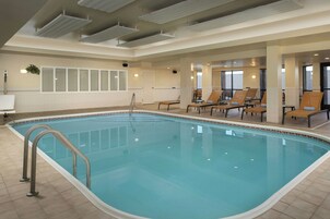 Una amplia piscina cubierta con suelo de baldosas, una escalera metálica y varias tumbonas alrededor del borde.