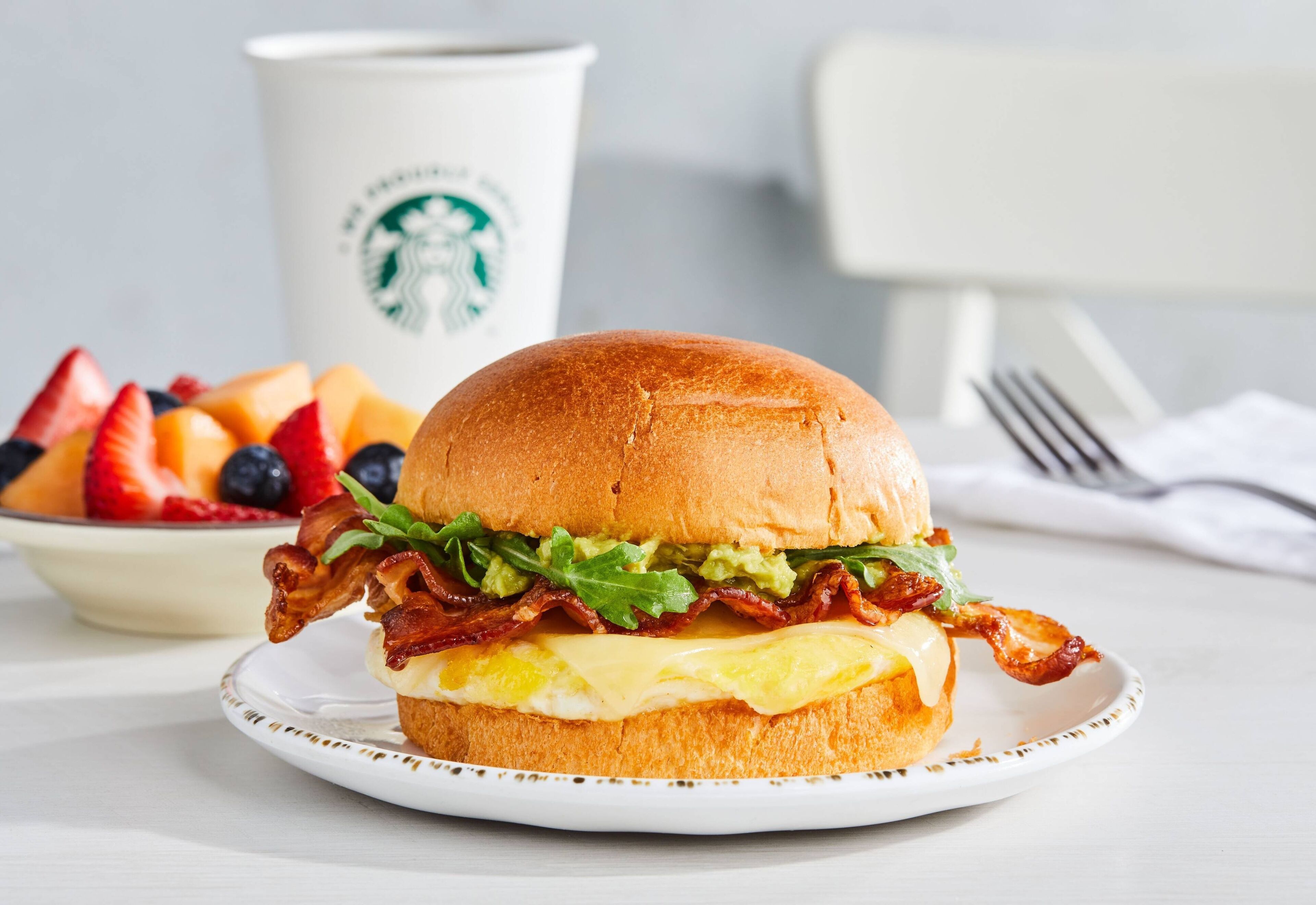 Un sandwich au petit-déjeuner sur une assiette, avec une tasse Starbucks en arrière-plan.