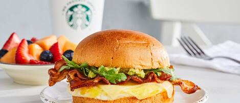 Un sándwich de desayuno en un plato, con una taza de Starbucks al fondo.