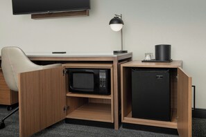 Een compacte hotelkamer met een ingebouwd bureau, een magnetron, een minibar, een bureaulamp en een flatscreen televisie.