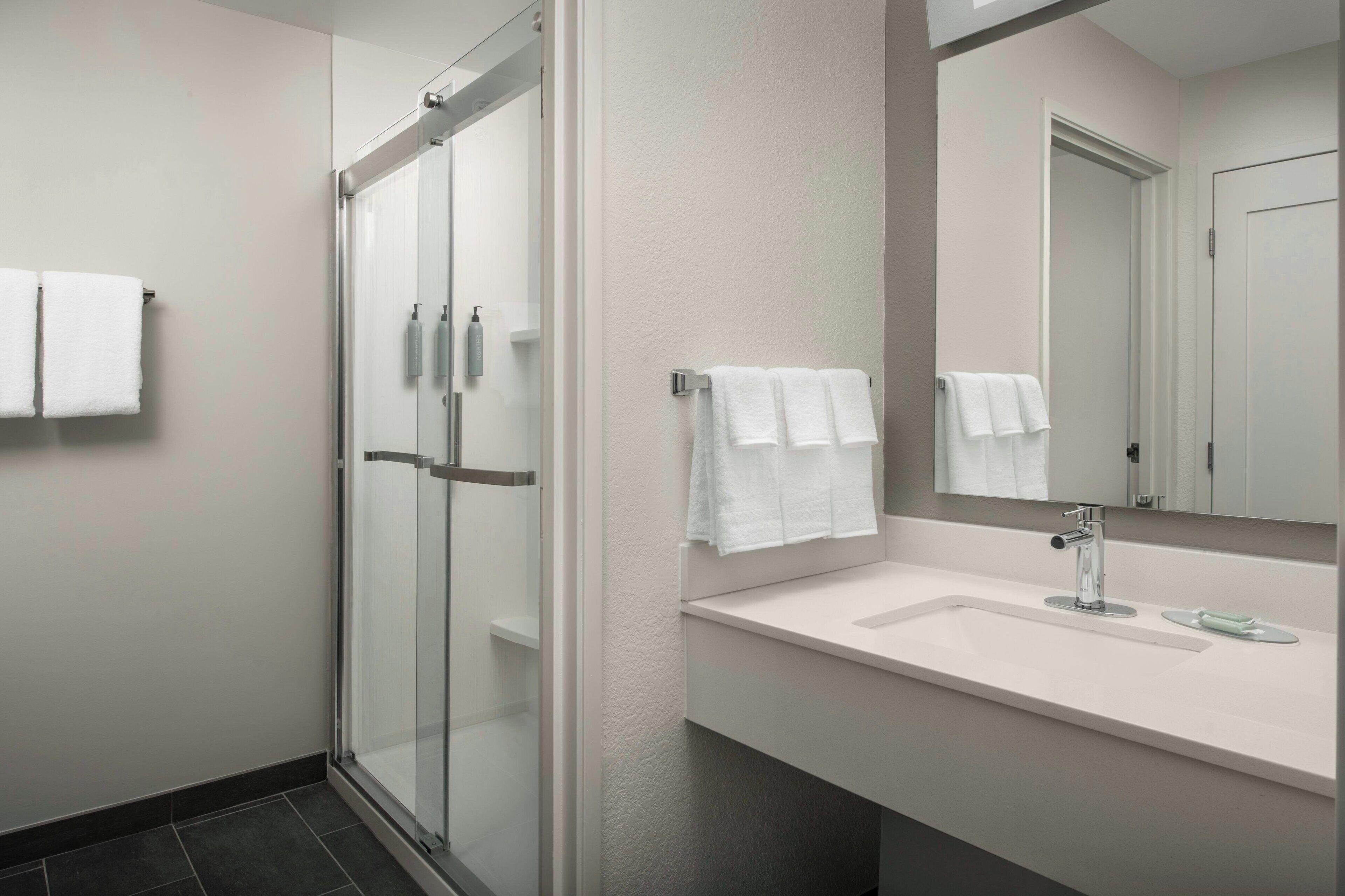 A modern bathroom with a glass shower enclosure, a white sink with a mirror, and two white towels on towel racks.