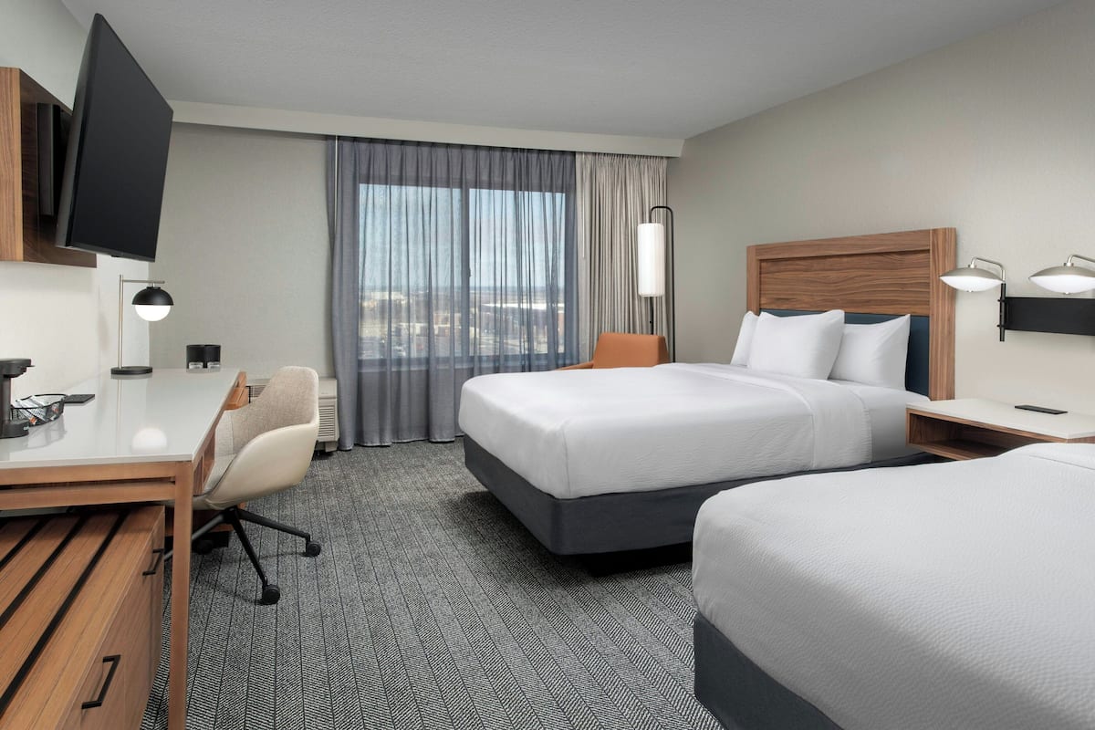 A hotel room with a bed, a desk, a chair, a TV, and a window with curtains.