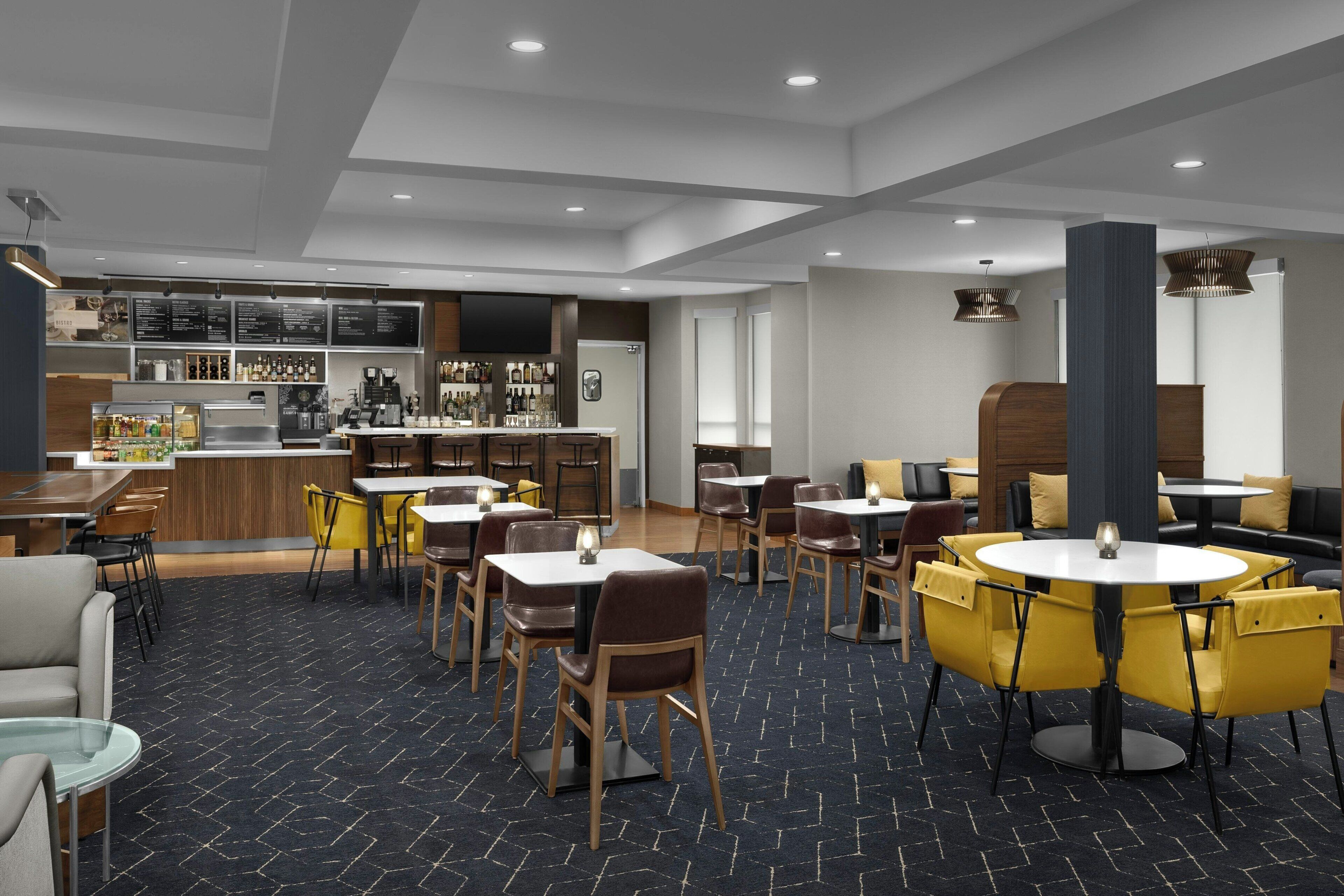 A modern restaurant with a bar area, multiple seating options including tables and chairs, and a patterned carpet.