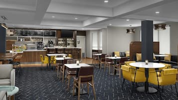 A modern restaurant with a bar area, multiple seating options including tables and chairs, and a patterned carpet.