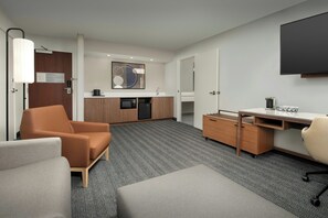 Een moderne hotelkamer met een bank, een bureau, een kitchenette en een flatscreen-tv.