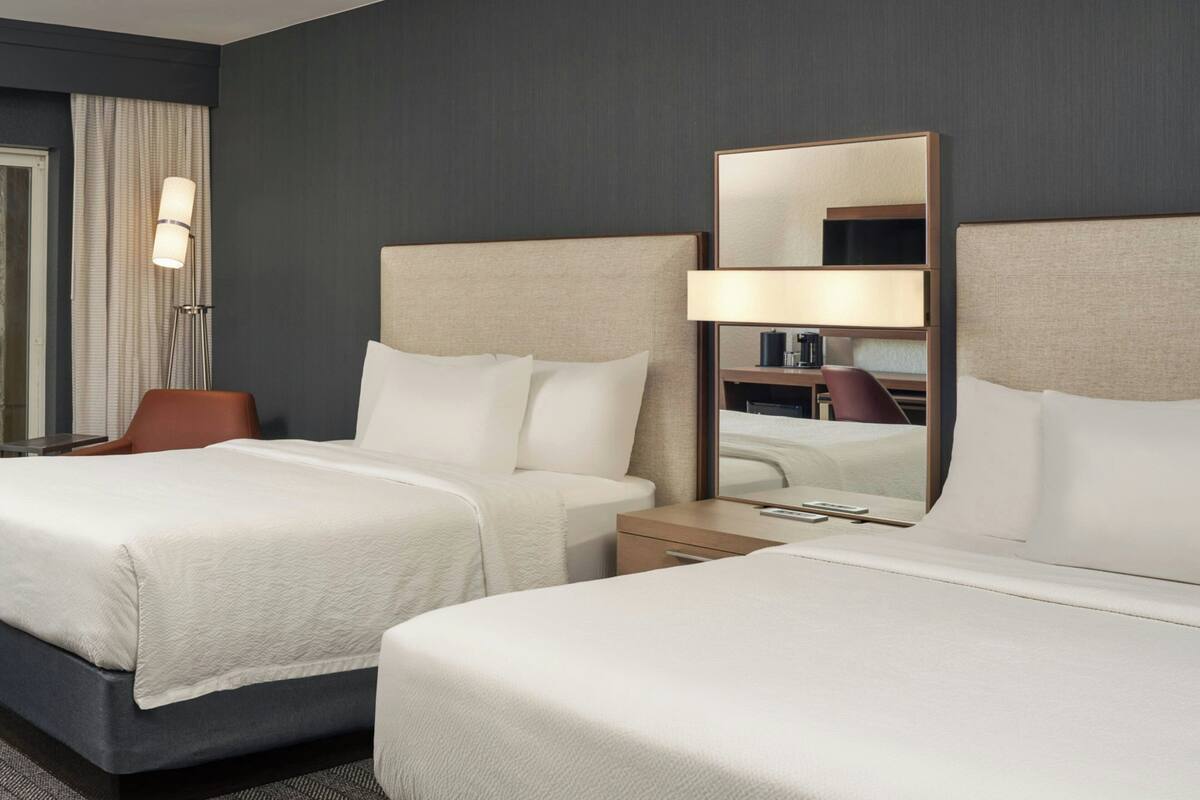 Une chambre d’hôtel avec deux lits, une table de chevet, une chaise, un bureau et un grand miroir.