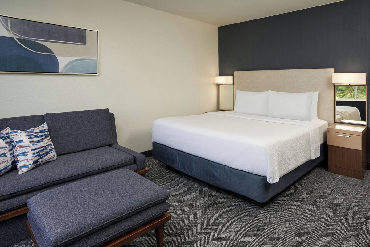 Une chambre d’hôtel avec un lit, un canapé, une table de chevet et une lampe.