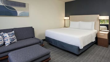 A hotel room with a bed, a sofa, a nightstand, and a lamp.